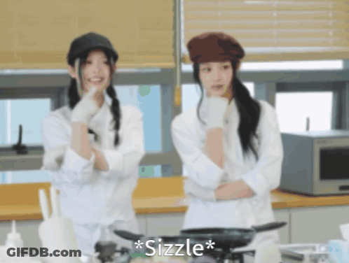 Two Women Are Standing In A Kitchen And The Word Sizzle Is On The Bottom Left GIF