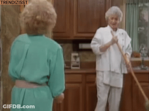 Two Women Are Standing In A Kitchen One Is Sweeping The Floor And The Other Is Looking At Her . GIF