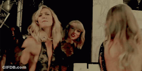 Two Women Are Standing In Front Of A Mirror Looking At Their Reflection GIF