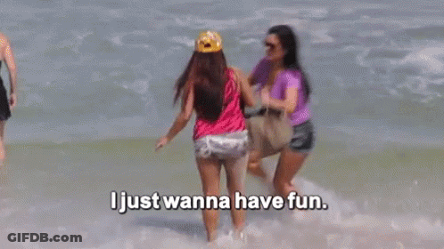 Two Women Are Standing In The Ocean With The Words `` I Just Wanna Have Fun '' Above Them . GIF
