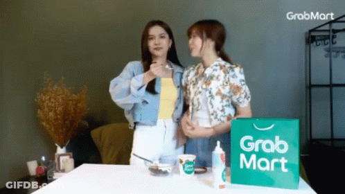Two Women Are Standing Next To A Grabmart Bag GIF