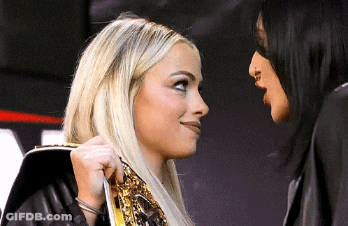 Two Women Are Standing Next To Each Other And Looking At Each Other . One Of The Women Is Wearing A Wrestling Belt . GIF
