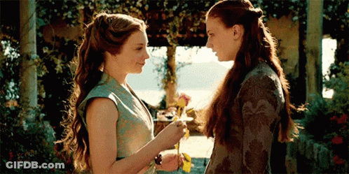 Two Women Are Standing Next To Each Other And Looking At Each Other . One Woman Is Holding A Flower . GIF