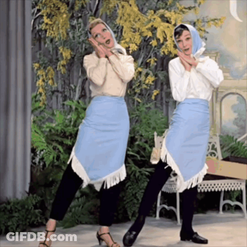Two Women Are Standing Next To Each Other And One Is Wearing A Blue Skirt With Fringe GIF