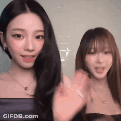 Two Women Are Standing Next To Each Other And One Of Them Is Waving Her Hand GIF