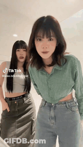 Two Women Are Standing Next To Each Other And One Of Them Is Wearing A Crop Top . GIF