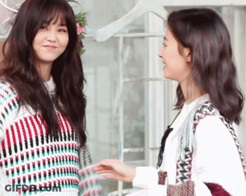Two Women Are Standing Next To Each Other Holding Hands And Smiling GIF