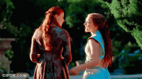 Two Women Are Standing Next To Each Other Holding Hands In A Garden . GIF