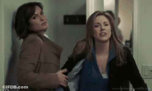 Two Women Are Standing Next To Each Other In A Hallway And One Of Them Is Holding The Other 'S Arm . GIF
