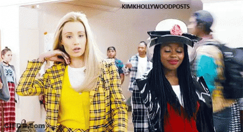 Two Women Are Standing Next To Each Other In A Hallway . One Of The Women Is Wearing A Yellow Plaid Shirt . GIF