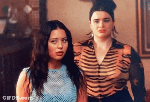 Two Women Are Standing Next To Each Other In A Room . One Of The Women Is Wearing A Tiger Print Shirt . GIF
