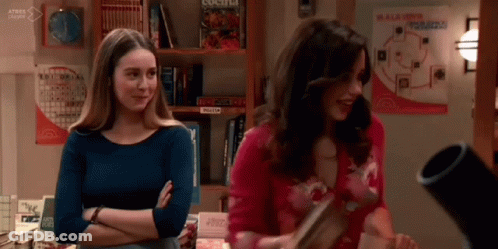 Two Women Are Standing Next To Each Other In A Room With A Bookshelf . GIF