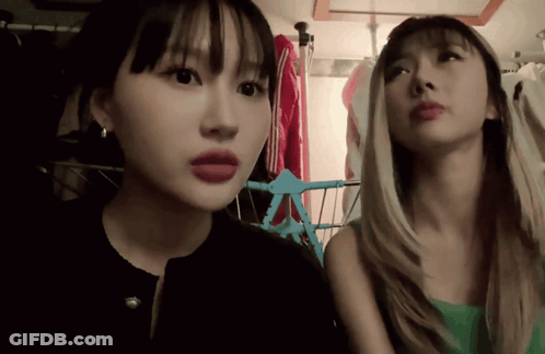 Two Women Are Standing Next To Each Other In A Room With Clothes Hanging On A Rack GIF