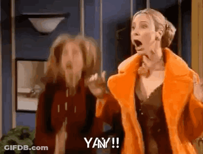 Two Women Are Standing Next To Each Other In A Room With Their Mouths Open And One Of Them Is Wearing An Orange Fur Coat GIF