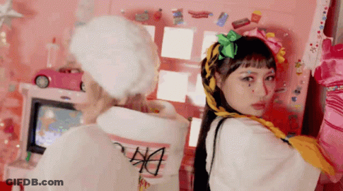 Two Women Are Standing Next To Each Other In Front Of A Pink Wall With Stickers On It . GIF