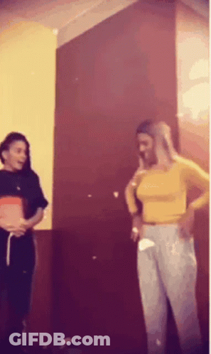 Two Women Are Standing Next To Each Other In Front Of A Red Wall . GIF
