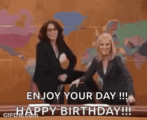 Two Women Are Standing Next To Each Other In Front Of A Table With The Words `` Enjoy Your Day ! '' GIF