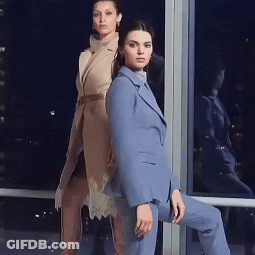 Two Women Are Standing Next To Each Other In Front Of A Window . One Of The Women Is Wearing A Blue Suit . GIF