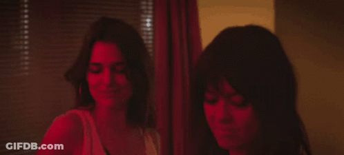 Two Women Are Standing Next To Each Other In Front Of A Window With Blinds . GIF