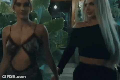 Two Women Are Standing Next To Each Other In Front Of Plants GIF