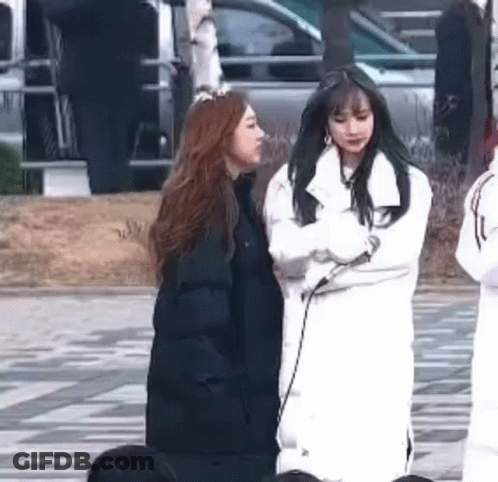 Two Women Are Standing Next To Each Other On A Sidewalk In Front Of A Car . GIF