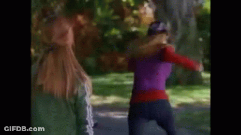Two Women Are Walking Down A Path In A Park . One Of The Women Is Wearing A Purple Top . GIF