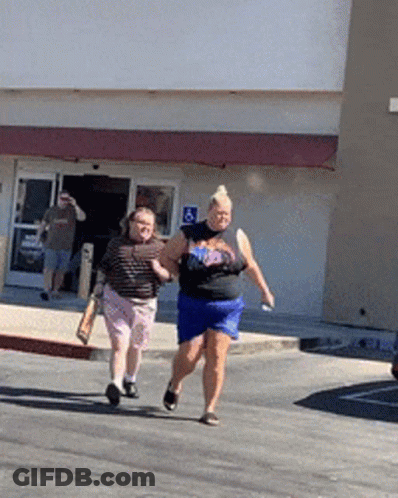 Two Women Are Walking Down The Street In Front Of A Building With A Handicap Sign GIF