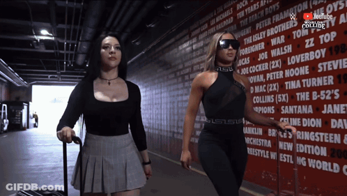 Two Women Are Walking In Front Of A Wall That Has A Youtube Logo On It GIF
