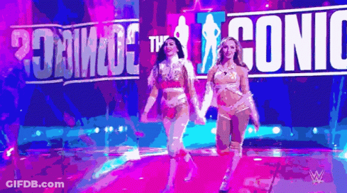 Two Women Are Walking On A Stage In Front Of A Sign That Says ' Iconic ' GIF