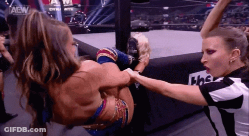 Two Women Are Wrestling In A Ring While A Referee Watches . GIF