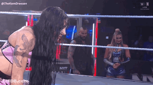 Two Women Are Wrestling In A Wrestling Ring While A Man Stands In The Background . GIF