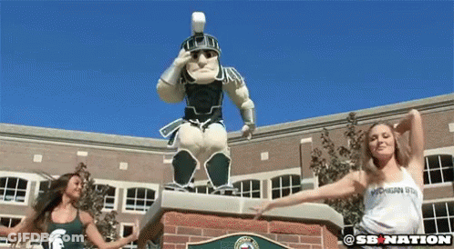 Two Women Dancing In Front Of Spartan Warrior Statue GIF