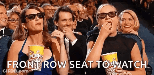Two Women Eating Popcorn In Front Of Crowd GIF