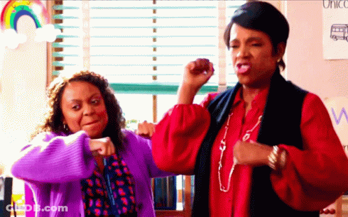 Two Women Flexing Muscles In Front Of Unicorn Sign GIF
