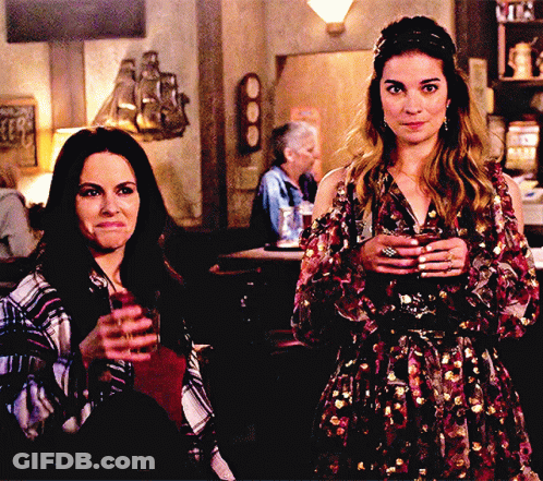 Two Women Holding Drinks At Bar GIF