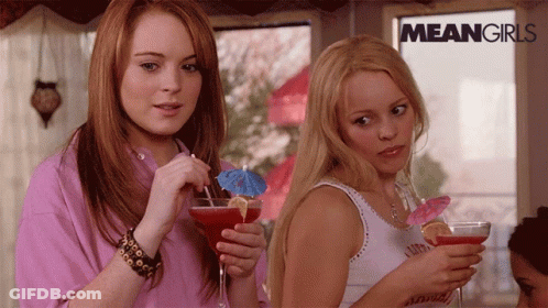 Two Women Holding Drinks In Front Of Mean Girls Sign GIF