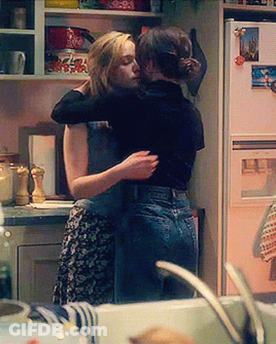 Two Women Hugging In A Kitchen With A Picture Of A City On The Refrigerator Door GIF