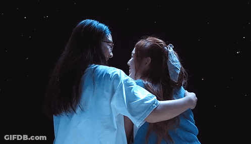 Two Women Hugging In Front Of Dark Background GIF