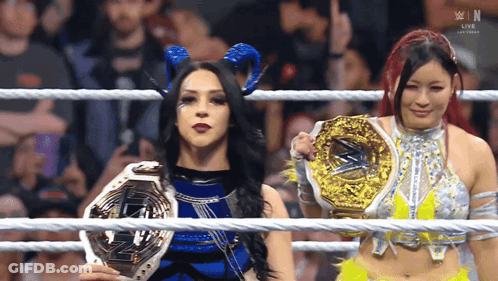 Two Women In A Wrestling Ring Holding Trophies With The Letters W In The Background GIF