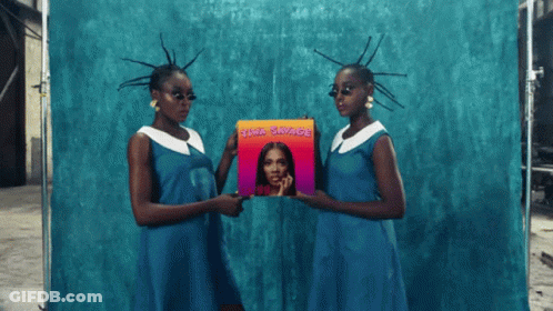 Two Women In Blue Dresses Holding A Cd Titled ' Awa Savage ' GIF