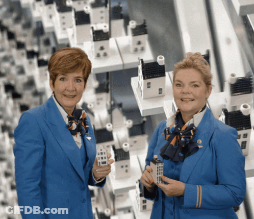 Two Women In Blue Uniforms Holding Miniature Houses GIF