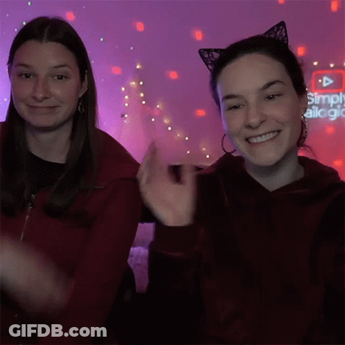 Two Women In Cat Ear Headbands In Front Of Simply Alegria Sign GIF