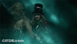 Two Women In Dark Room One Wearing Top Hat GIF