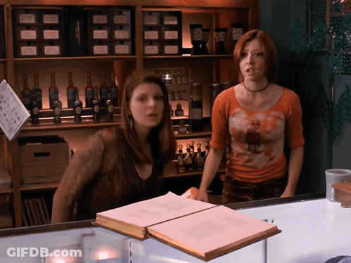 Two Women In Front Of Shelf With Bottles And Sign Saying A GIF