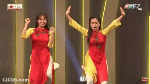 Two Women In Red And Yellow Dresses On Stage With Arms Up GIF