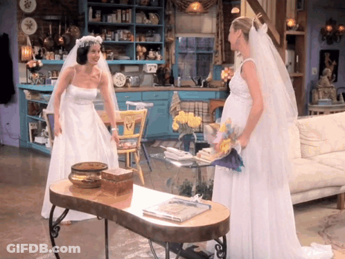 Two Women In Wedding Dresses Standing Next To Each Other In A Living Room GIF