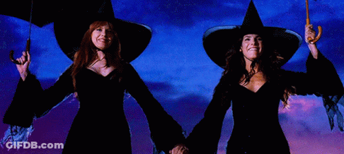 Two Women In Witch Hats Holding Umbrellas In Front Of A Blue Sky GIF