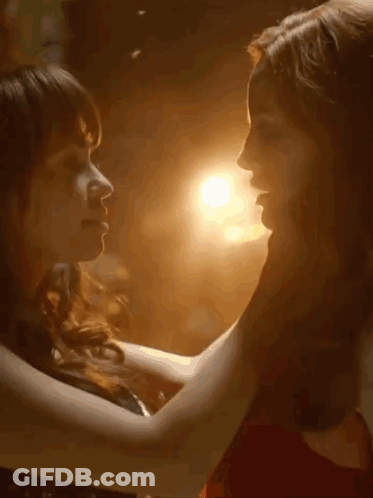 Two Women Kissing In Dark Room With Light Behind Them GIF