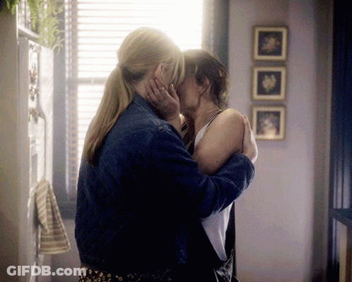 Two Women Kissing In Front Of A Window With Three Pictures On The Wall Behind Them GIF