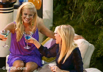 Two Women On Couch Drinking Cocktails And Smiling GIF